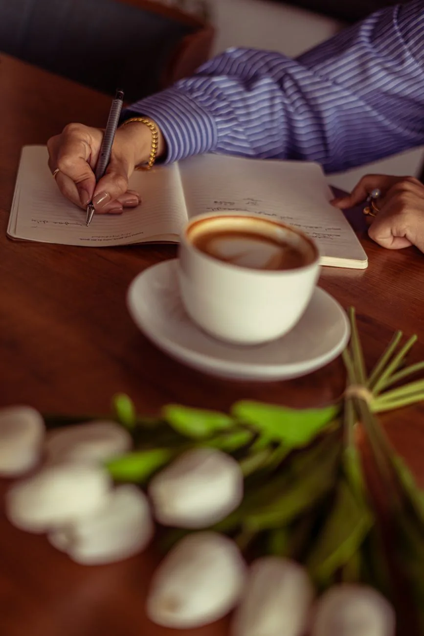 Woman writing in journal with coffee and flowers